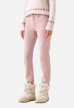 Persoon die lichtroze broek draagt, witte winterlaarzen met bontkraag en een witte trui met roze en bruine patronen op mouwen en zoom.