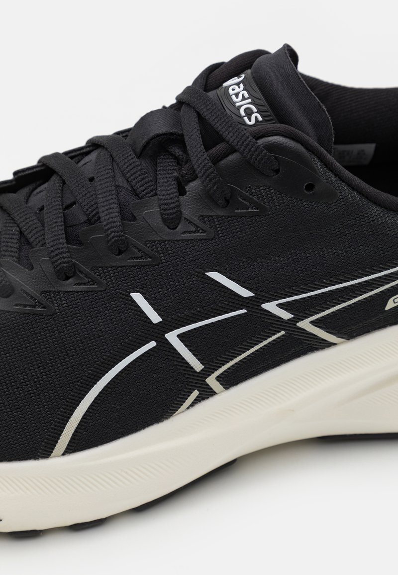 Zapatilla deportiva negra con parte superior texturizada, que presenta acentos blancos y un diseño aerodinámico. Cierre con cordones y cuello acolchado. Suela ligera.