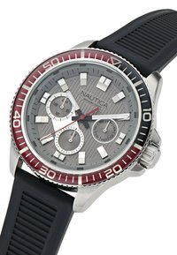 Reloj Nautica con caja de acero inoxidable, esfera texturizada gris, bisel rojo, correa de goma y tres subdiales de cronógrafo. Resistente al agua hasta 100m.