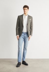 Sacou gri, cămașă albă, blugi deschiși la culoare, mocasini negri. Sacoul are o textură subtilă și două buzunare în față.