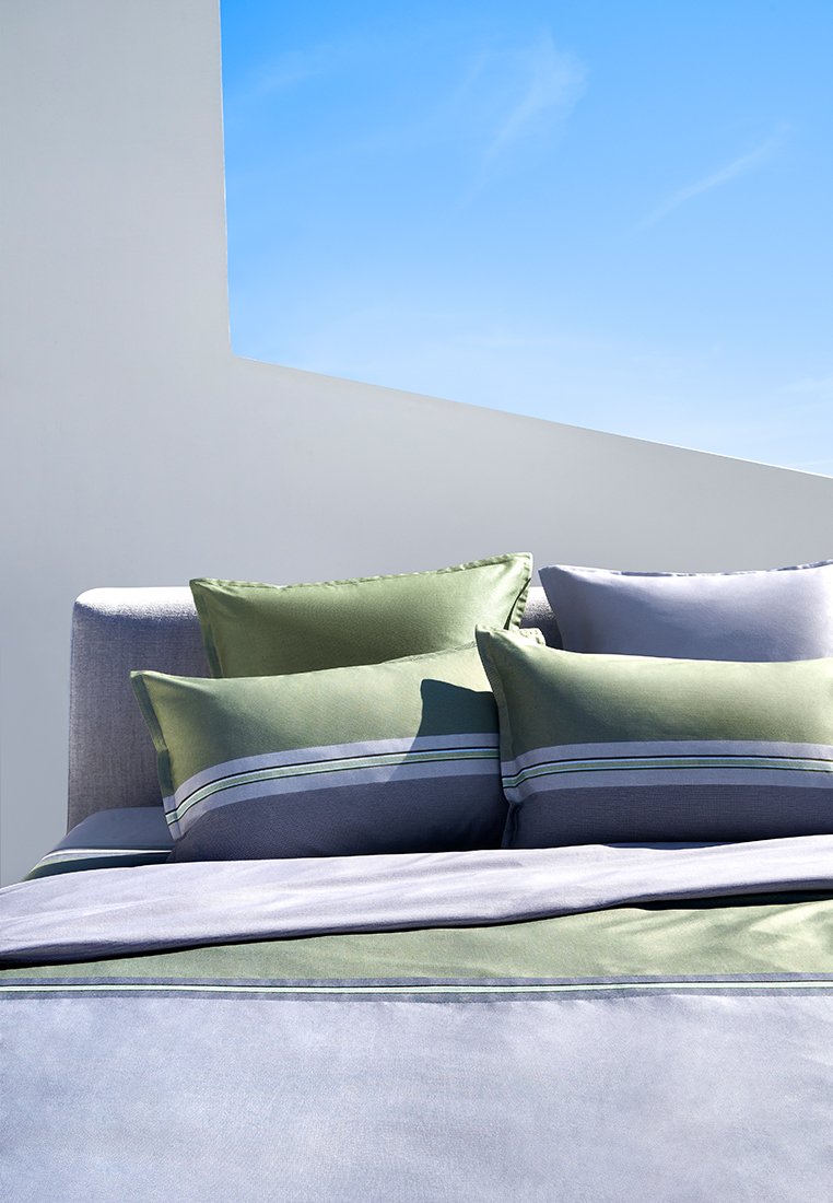 Ensemble de literie doux avec un tissu gris et des oreillers d'accent verts. Les oreillers ont des motifs rayés ; leur texture lisse et leur forme rectangulaire rehaussent le design.