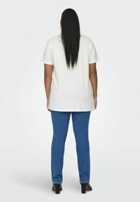 Tricou alb din bumbac, cu mâneci scurte, asortat cu blugi albaștri. Tricoul are o croială lejeră și se termină sub șolduri.