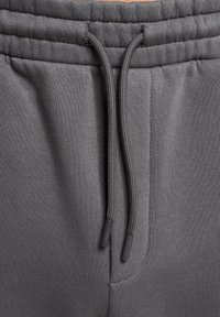 Grå sweatpants med snoreliv, der har en glat tekstur og to sidelommer. Snørebåndet har sorte plastikspidser.