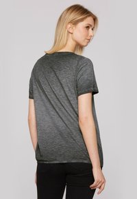 Szara koszulka z miękkim, teksturowanym wykończeniem i krótkimi rękawami, z okrągłym dekoltem i luźnym krojem, w zestawie z czarnymi dżinsami.