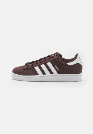 Brązowy zamszowy sneaker Adidas Campus z białymi paskami, białą zakładką na pięcie i białą gumową podeszwą, pokazany z profilu lewej strony.