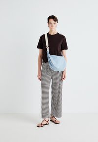 Light blue denim shoulder bag with cream strap, paired with a black t-shirt and black and white striped wide-leg pants. Flat sandals worn.