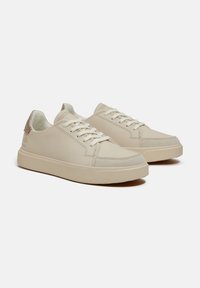 Sneakers in pelle beige con tomaia liscia, punta rotonda e chiusura con lacci. Dettagli texturizzati sul tallone e logo sul lato.