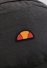 Tissu noir avec un petit patch logo présentant un demi-cercle divisé en une partie orange et deux parties rouges soulignées en noir.