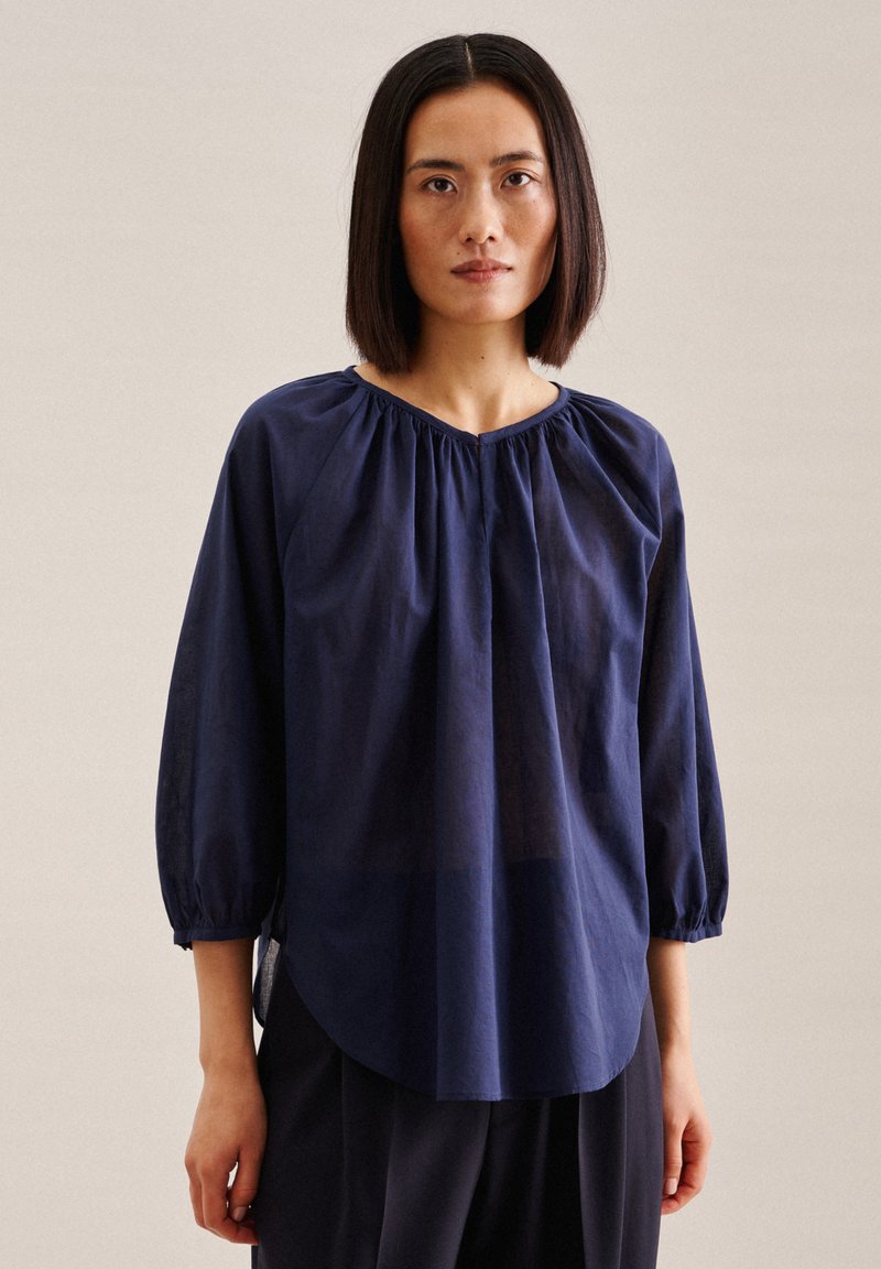 Himmelblau, leichtes Blusenshirt mit rundem Halsausschnitt, raffiniertem Detail an den Schultern und langen, leicht puffigen Ärmeln.