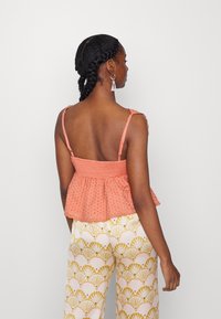 Top sem mangas em cor pêssego com corpete franzido e padrão texturizado, combinado com calças largas com um design de concha amarela.