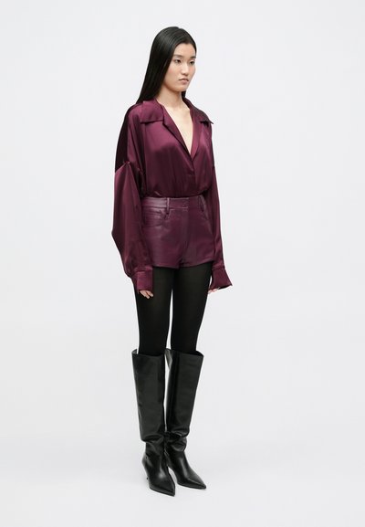 Bordo satenasta bluza z globokim V-izrezom, dolgimi rokavi, kombinirana z visokim usnjenim kratkim hlačami, črnimi nogavicami in črnimi škornji do kolen.