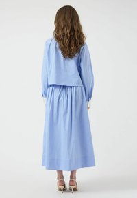 Conjunto de dos piezas en azul claro que presenta una blusa corta con mangas largas y una falda de cintura alta y larga, fabricada con tejido texturizado.