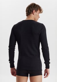 Sort langærmet skjorte med rund hals, tætsiddende pasform, ribbede manchetter og glat tekstur, parret med sorte boxershorts.