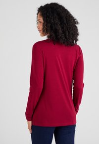 Bordeaux langemouwen overhemd van zachte stof, met een ronde halslijn en een aansluitend ontwerp, gecombineerd met donkerblauwe jeans.