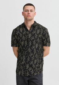 Chemise noire à manches courtes avec un motif de feuilles beiges, design à boutons et col. Texture lisse et coupe décontractée.