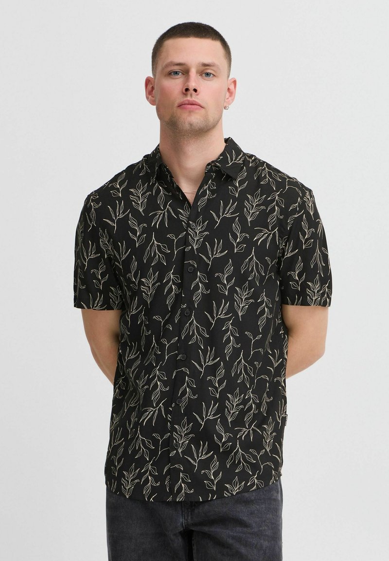 Chemise noire à manches courtes avec un motif de feuilles beiges, design à boutons et col. Texture lisse et coupe décontractée.