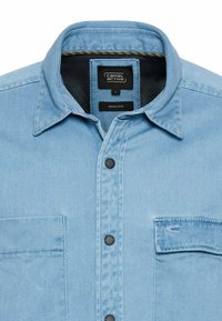 Lichtblauw denim shirt met een klassieke kraag, zwarte knopen, een borstzak en een label dat aan de binnenkant 'indigo geverfd' aangeeft.