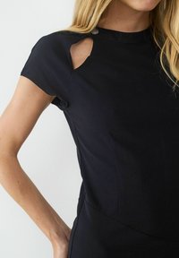 Czarna sukienka z krótkim rękawem, z wysokim dekoltem, bocznym wycięciem i gładką fakturą. Posiada ozdobny guzik przy ramieniu.