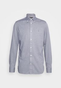 Camisa de manga larga con botones en tela azul claro, que presenta un cuello clásico, botones blancos y un pequeño logo en el pecho.