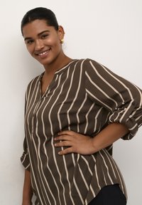 Brown and beige striped blouse with a v-neck and buttoned cuffs. Soft fabric and relaxed fit, featuring rolled sleeves and side slits.