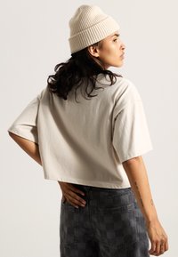 Beige cropped t-shirt with short sleeves, made of soft cotton, paired with dark checkered pants and a light ribbed knit beanie.
