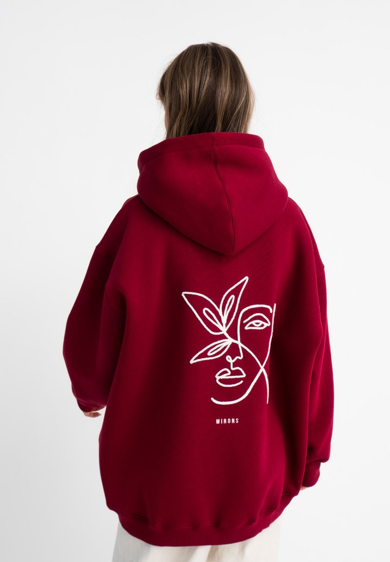 Rode oversized hoodie met een witte lijntekening van een gezicht en bladeren op de achterkant. Heeft een grote capuchon en geribde boorden.