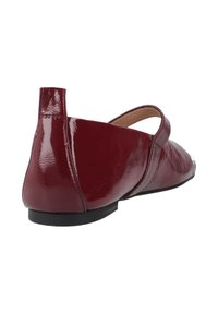 Scarpa piatta in vernice color bordeaux con tacco basso, punta arrotondata e cinturino laterale. Texture liscia con una finitura lucida.
