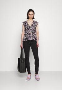 Blusa preta floral com mangas em babados, apresentando padrões roxos e verdes. Combinada com jeans pretos e saltos plataforma lilás.