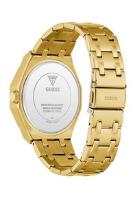 Montre-bracelet en métal doré avec un bracelet à maillons, fermoir gravé GUESS, et dos en acier inoxydable détaillant la résistance à l'eau et le mouvement japonais.