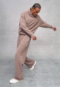 Sudadera marrón de corte amplio, pantalones de chándal marrones a juego y zapatillas blancas. Estilo casual, textura suave y detalles de marca mínimos.