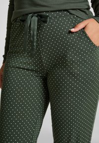 Groene broek met stippen in een zachte textuur, voorzien van een satijnen strikband en zakken. De stof heeft een subtiel geribbeld patroon.