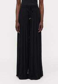 Pantalon large noir taille haute en tissu texturé, avec une taille à cordon de serrage et des accessoires dorés au niveau des extrémités du cordon.