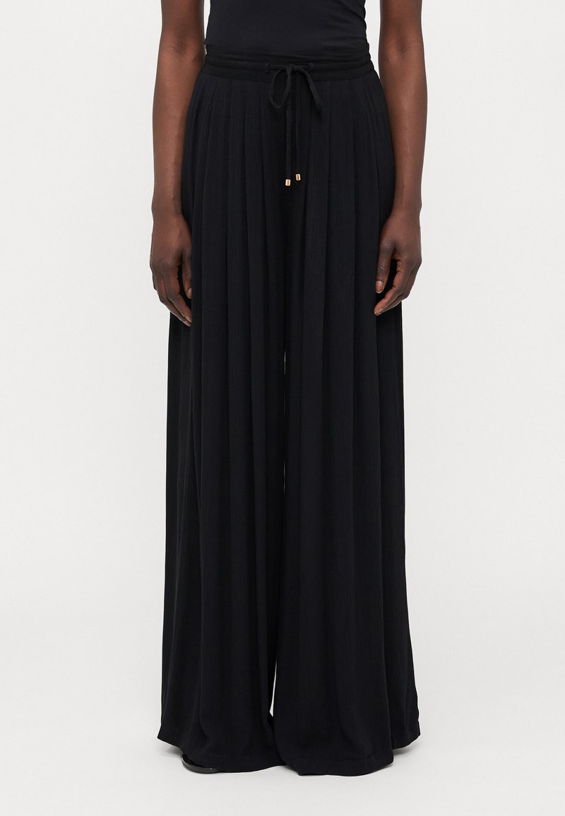 Pantalon large noir taille haute en tissu texturé, avec une taille à cordon de serrage et des accessoires dorés au niveau des extrémités du cordon.