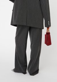Costume gris à rayures avec un pantalon large et un long blazer, associé à un sac à main en perles rouges avec des accents circulaires.