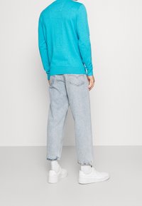 Pull bleu clair avec poignets côtelés, associé à un jean ample de lavage clair et des baskets blanches. Le pull présente un détail de texture subtil au dos.