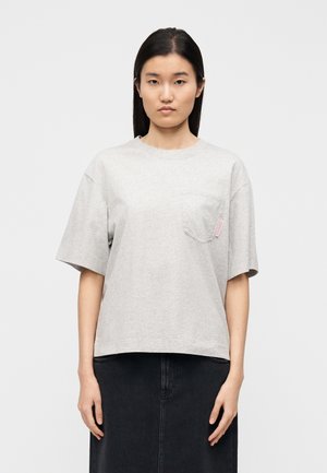 Szara koszulka z krótkim rękawem, z kieszonką i różową naszywką z logo. Miękka tkanina i luźny krój, lekko opadająca poniżej talii.