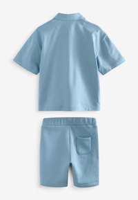 Ljusblå pikétröja med korta ärmar och matchande shorts. Tröjan har krage och shortsen har en bakficka. Mjukt tyg med slät textur.