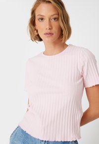 Lyserød ribbet t-shirt med korte ærmer, rund halsudskæring og bølget kant. Stofmet har en blød tekstur med et subtilt mønster.