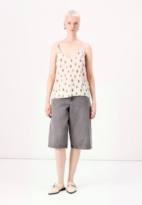 Beige ilmanhihaista toppia, jossa on timanttikuvio, on yhdistetty harmaisiin farkkushortseihin. Mallilla on kevyet kengät. Yksinkertainen muotoilu, neutraalit värit.