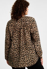 Leopard print langemouwen shirt met een verzamelde achterkant, met een tan en zwarte kleurenschema op een zachte stof.