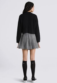 Suéter negro corto, falda plisada con patrón de pata de gallo, calcetas negras hasta la rodilla y zapatillas negras. Texturas suaves y colores en contraste.