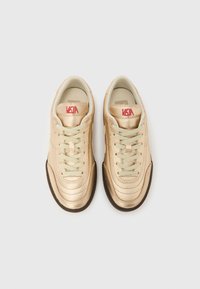 Χρυσά μεταλλικά αθλητικά παπούτσια με λεία υφή, με κρέμα κορδόνια, στρογγυλερή μύτη και καφέ λαστιχένια σόλα. Κόκκινο λογότυπο "VEJA" στη γλώσσα του παπουτσιού.