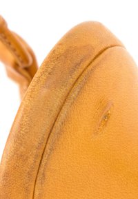 Gros plan d’un coin usé d’un sac en cuir marron clair avec des marques d’usure visibles et des coutures sur fond blanc.