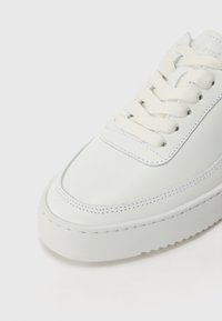 Vita lädersneaker med en slät yta, rund tå, platta vita skosnören och ton-i-ton sömmar. Har en tjock gummisula.