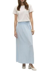 Jupe maxi bleu clair avec une taille smockée, associée à un t-shirt crème avec une poche texturée. Le mannequin porte des chaussures à talons carrés beige.