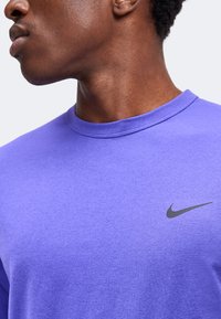 Κοντινό ενός ατόμου που φοράει μωβ μπλούζα Nike, με εμφανές το λαιμόκομμα και το μαύρο λογότυπο Nike στο στήθος.
