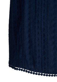 Tessuto blu navy con un motivo testurizzato caratterizzato da strisce verticali e piccole aperture ovali, rifinito con un bordo a pompon scallopato all'orlo.