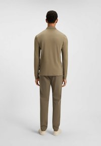 Langsleeve polo in olijfgroene stof, gecombineerd met bijpassende broek. Vloeiende textuur, relaxte pasvorm, minimalistisch ontwerp en eenvoudige kraag.