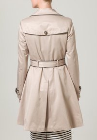 Beżowy płaszcz trencz z zakładką z tyłu, paskiem w talii i detalem z guzikami na kołnierzu. Charakteryzuje się gładką, błyszczącą fakturą.