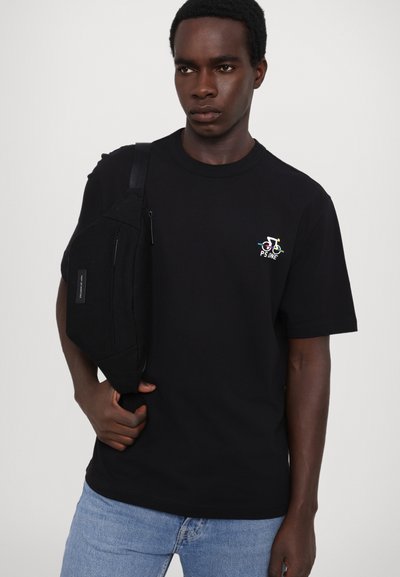 Czarny bawełniany t-shirt z okrągłym dekoltem, z małym wielokolorowym wzorem na lewej piersi. Osoba nosi czarną torbę na ramię.